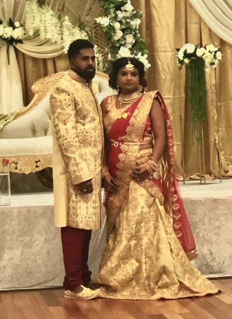 Sri Lankan couple in traditional wedding attire in front of an ornate floral stage