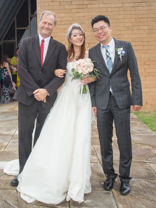 Bride holding her bouquet between two groomsmen in front of The Coast Chapel, Little Bay NSW