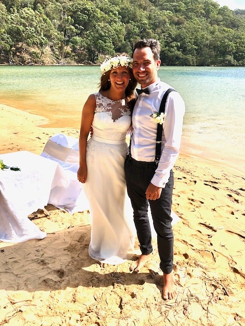 Bride in a floral crown and groom in suspenders, barefoot on a sandy beach on the Hawkesbury River, NSW