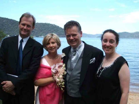 Wedding couple and two guests posing by the water with green hills on Dangar Island, NSW
