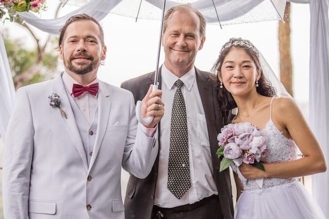 Groom, celebrant with an umbrella, and bride at a relaxed outdoor ceremony at the Bible Garden, Palm Beach